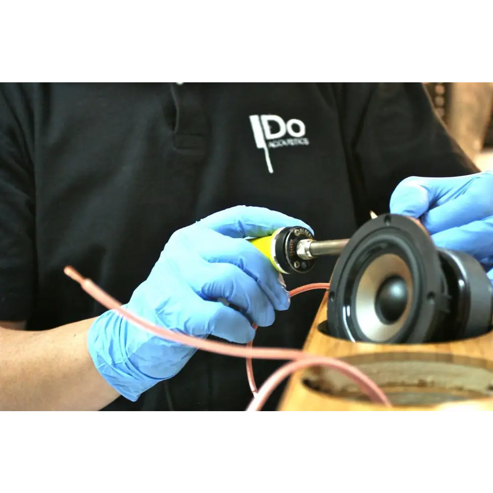Mensch soldert Lautsprecher für Do Acoustics 202 Wood Paar Demomodell mit blauen Handschuhen